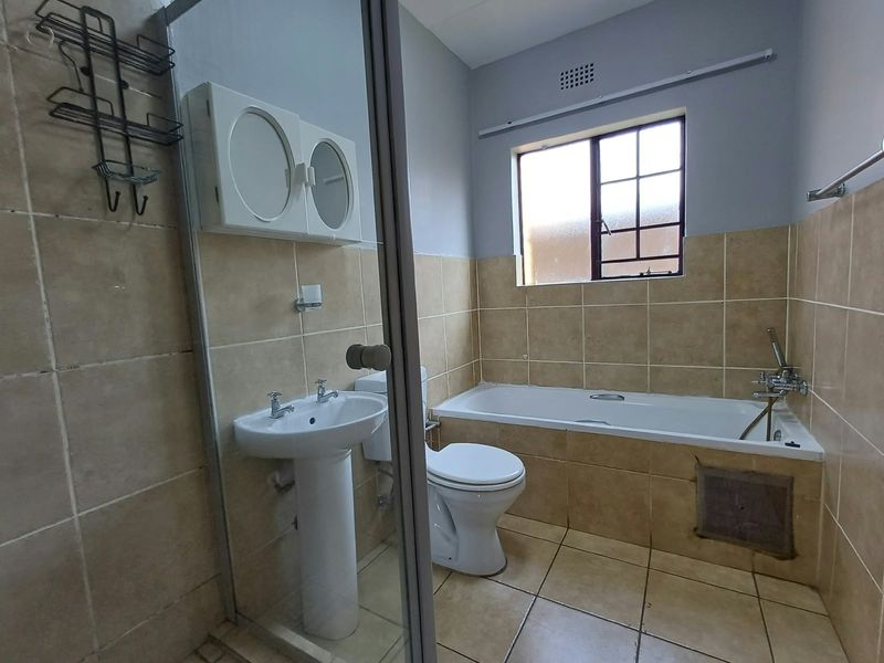 A functional bathroom featuring a pedestal basin, toilet, and bathtub with tiled finishes, requiring minor maintenance to the bathtub apron.