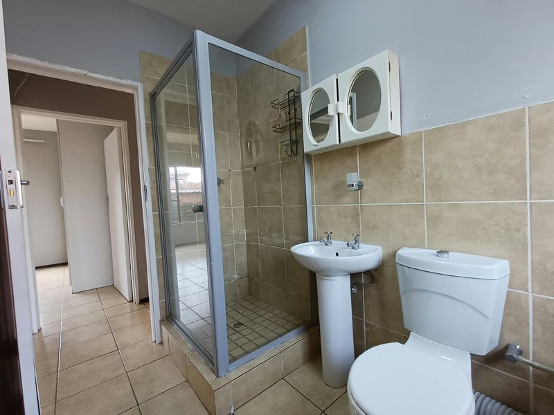 A functional bathroom featuring a glass shower enclosure, pedestal basin, and toilet with neutral wall and floor tiling.