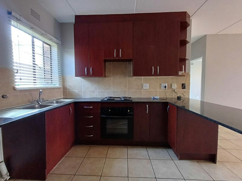 A functional kitchen featuring dark wood cabinetry, granite countertops, a built-in oven and hob, and tiled flooring with a neutral backsplash.