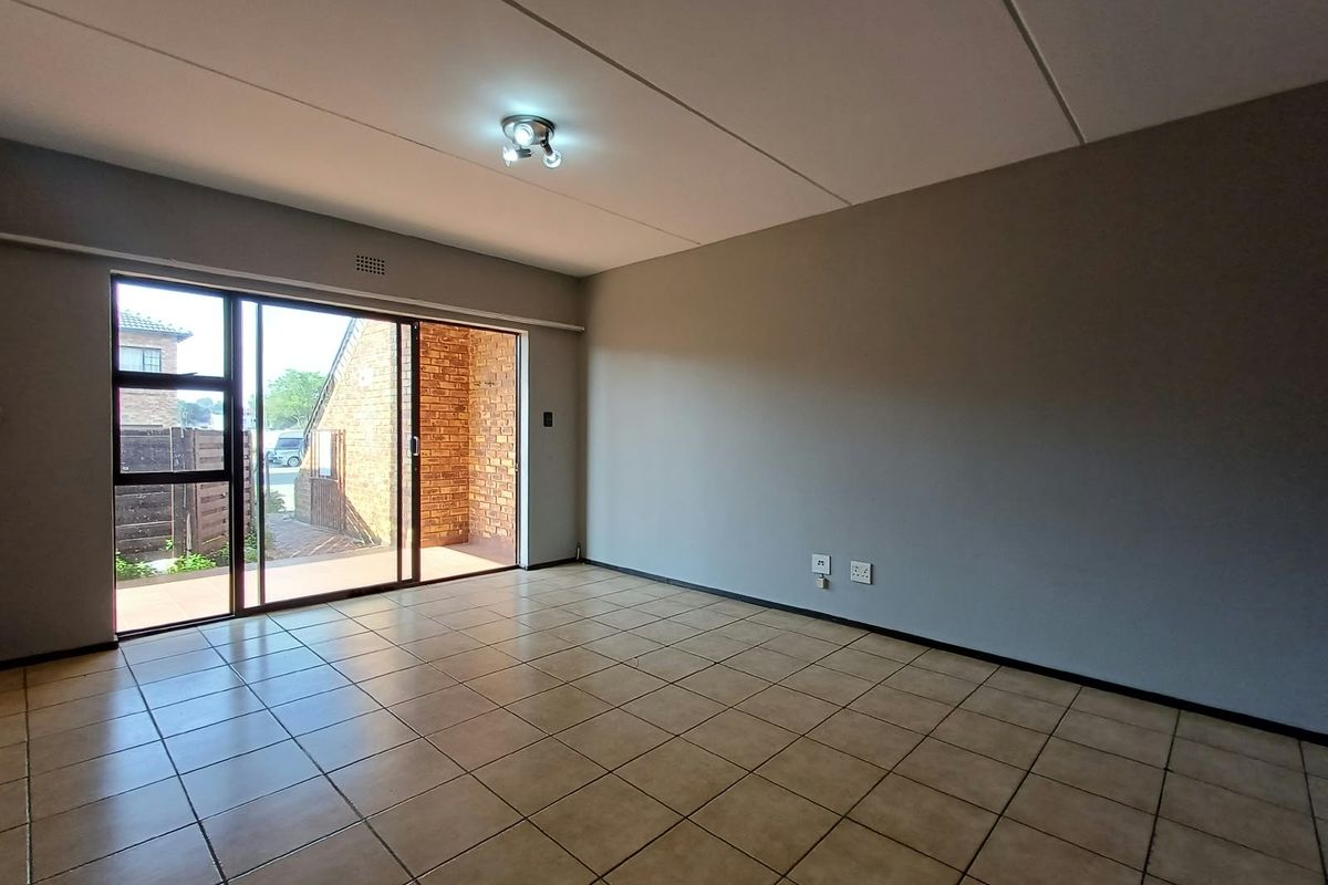 A spacious, empty living area featuring neutral walls, tiled flooring, and a large sliding glass door providing access to an outdoor patio space.