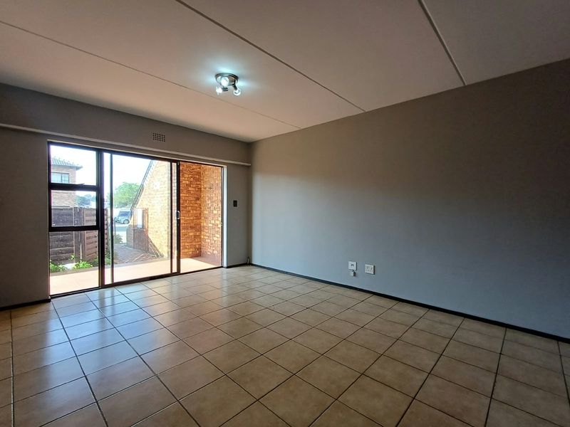 A spacious, empty living area featuring neutral walls, tiled flooring, and a large sliding glass door providing access to an outdoor patio space.