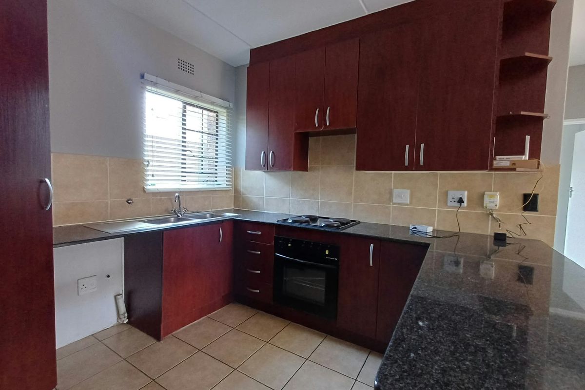 A functional kitchen featuring dark wood cabinetry, granite countertops, a built-in oven and hob, and tiled flooring with a neutral backsplash.