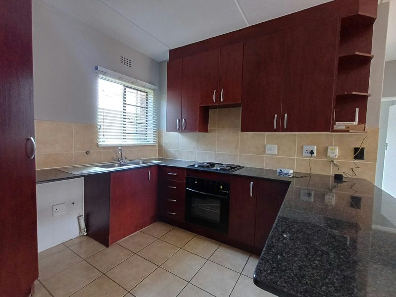 A functional kitchen featuring dark wood cabinetry, granite countertops, a built-in oven and hob, and tiled flooring with a neutral backsplash.