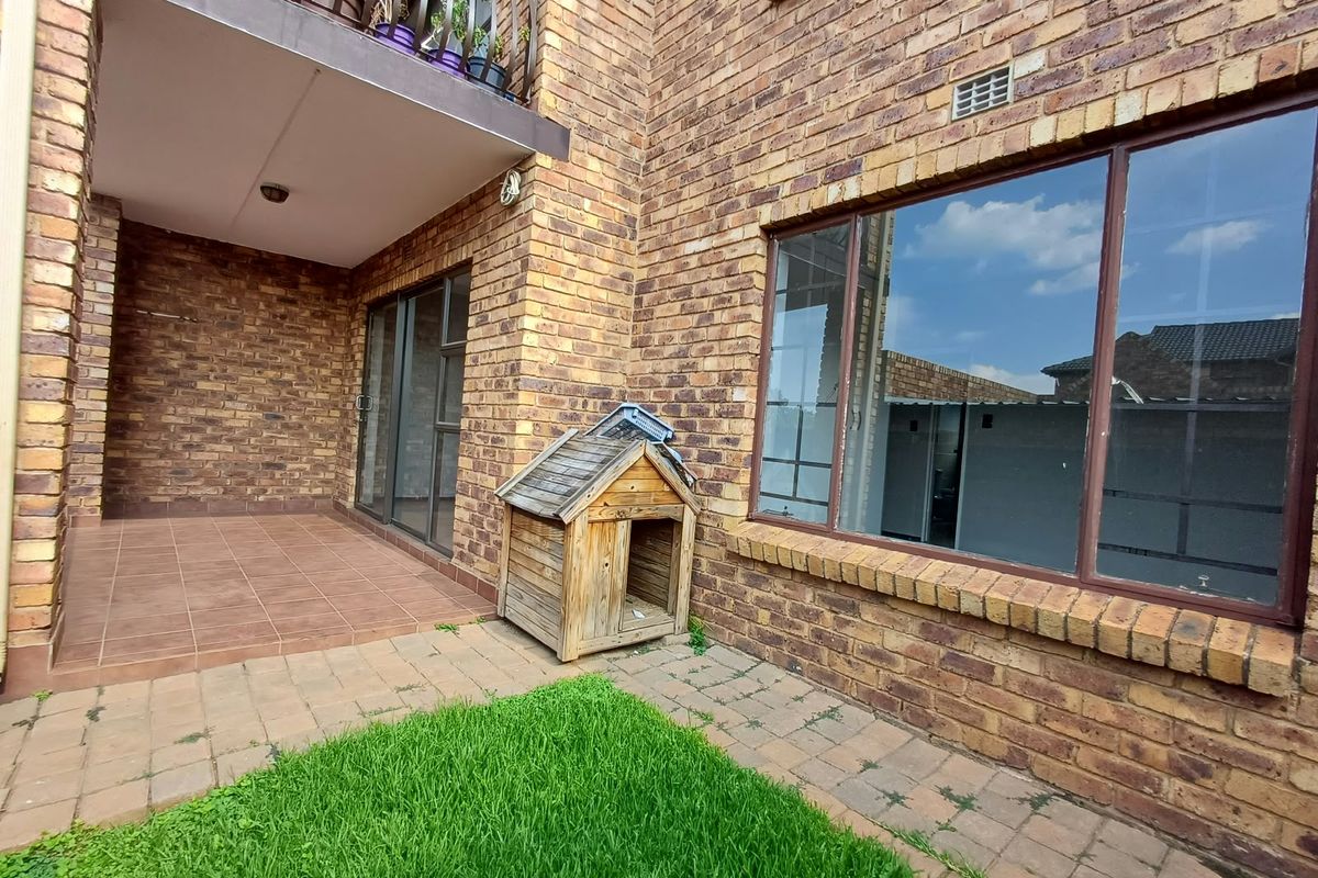 Rear exterior view of the apartment featuring a face brick facade, tiled patio area, paved walkway, and large aluminium-framed windows.