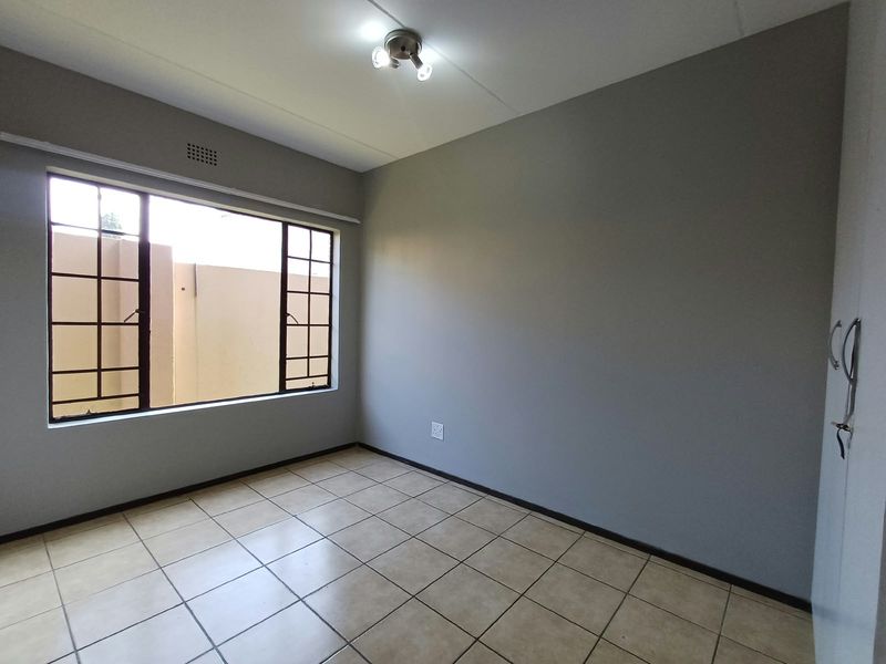 A clean, empty bedroom featuring neutral grey walls, tiled flooring, and a built-in cupboard, offering a versatile space ready for personalization.