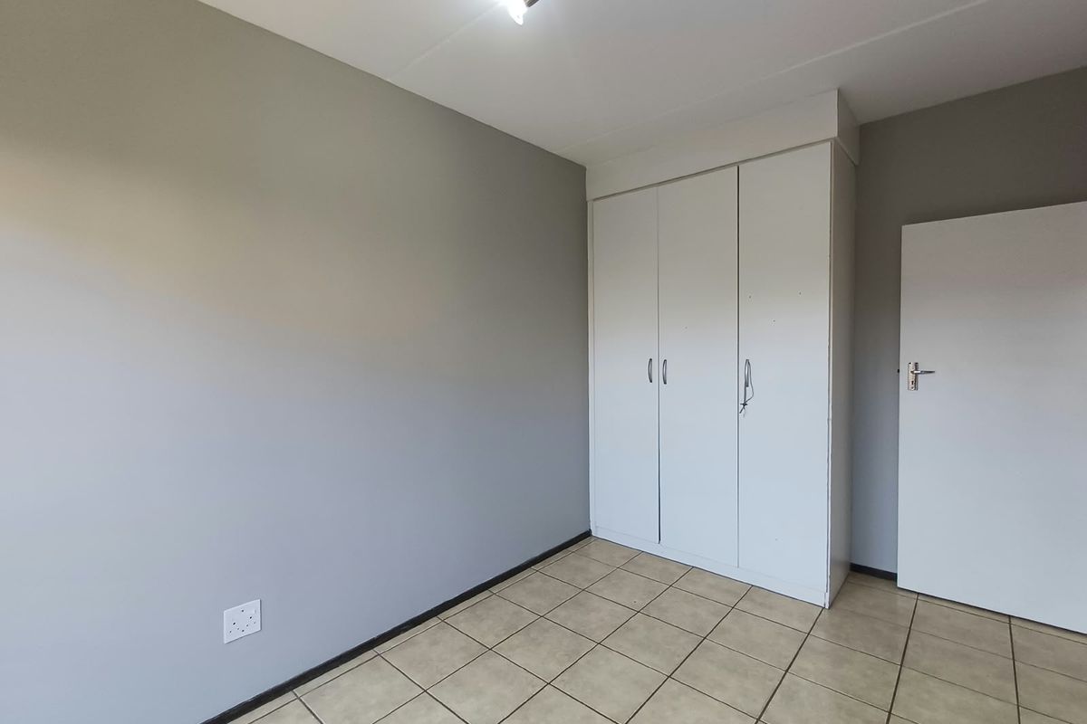 A clean, empty bedroom featuring neutral grey walls, tiled flooring, and built-in white cupboards.