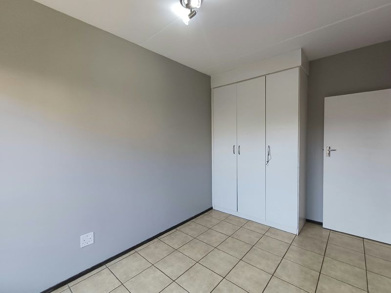 A clean, empty bedroom featuring neutral grey walls, tiled flooring, and built-in white cupboards.