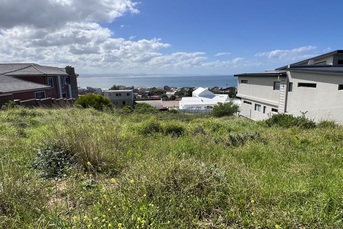 A vacant residential plot featuring a sloped landscape with expansive coastal and ocean views, surrounded by established residential properties.