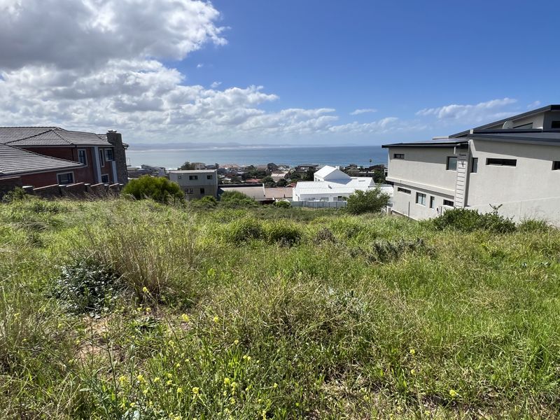 A vacant residential plot featuring a sloped landscape with expansive coastal and ocean views, surrounded by established residential properties.