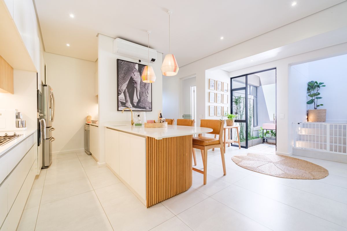 Modern kitchen featuring a central island with slatted timber detailing, stone countertops, recessed lighting, and seamless access to an outdoor patio area.