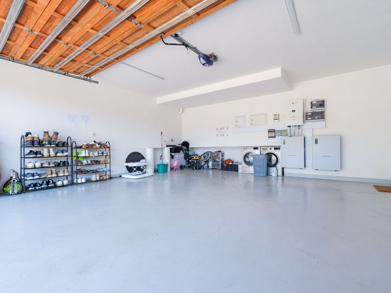 Spacious double garage featuring an epoxy-coated floor, integrated solar inverter and battery storage system, and dedicated laundry plumbing connections.