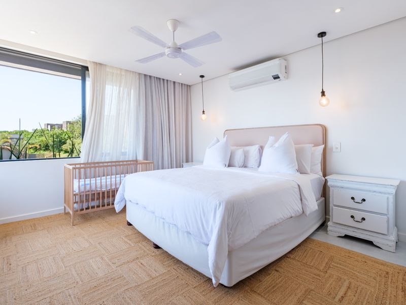 A bright and modern bedroom featuring a ceiling fan, split-system air conditioning, and large windows that provide ample natural light.