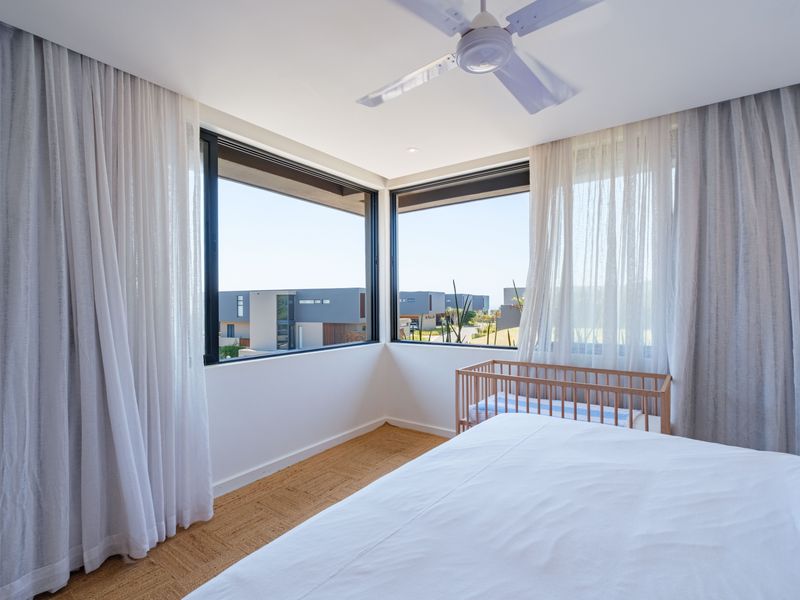 A bright, modern bedroom featuring corner windows with natural light, a ceiling fan, and neutral finishes.
