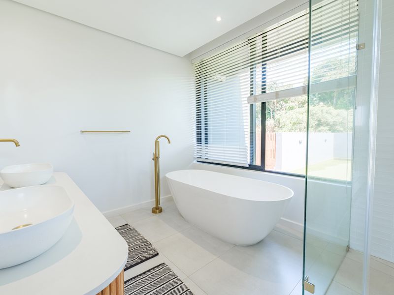 Modern bathroom featuring a sleek freestanding bathtub, double vanity with vessel sinks, brass fixtures, and a glass-enclosed shower with natural light.