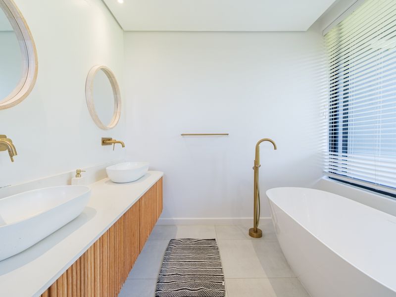 Modern bathroom featuring a double vanity with vessel sinks, brass fixtures, and a sleek freestanding bathtub with a floor-mounted filler.
