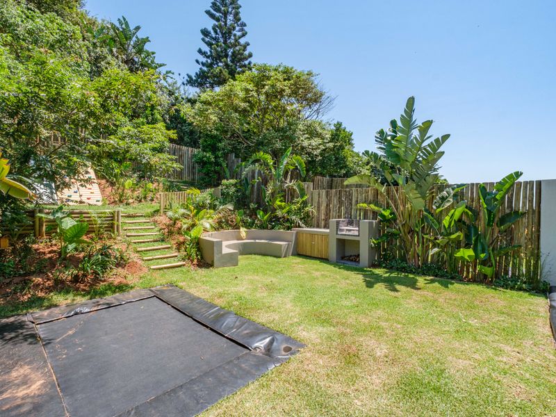 A landscaped garden featuring a built-in braai area, concrete bench seating, and timber steps leading up a terraced slope with mature greenery.