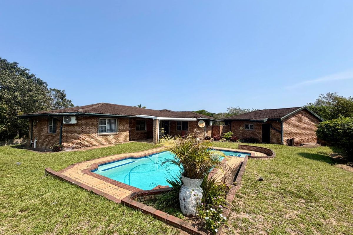 Rear view of the property featuring a brick exterior, tiled roof, and a swimming pool set within a grassed garden area.