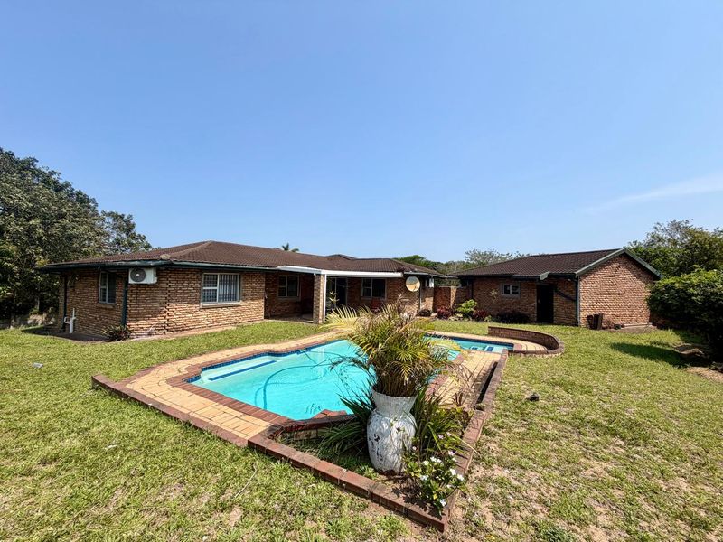 Rear view of the property featuring a brick exterior, tiled roof, and a swimming pool set within a grassed garden area.