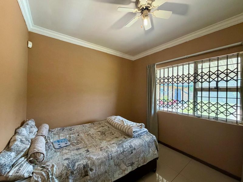 A bedroom featuring tiled flooring, a ceiling fan, and a window fitted with a security gate.