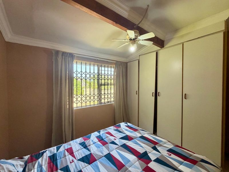 A bedroom featuring built-in cupboards, a ceiling fan, and a security gate on the window, providing functional storage and basic security.