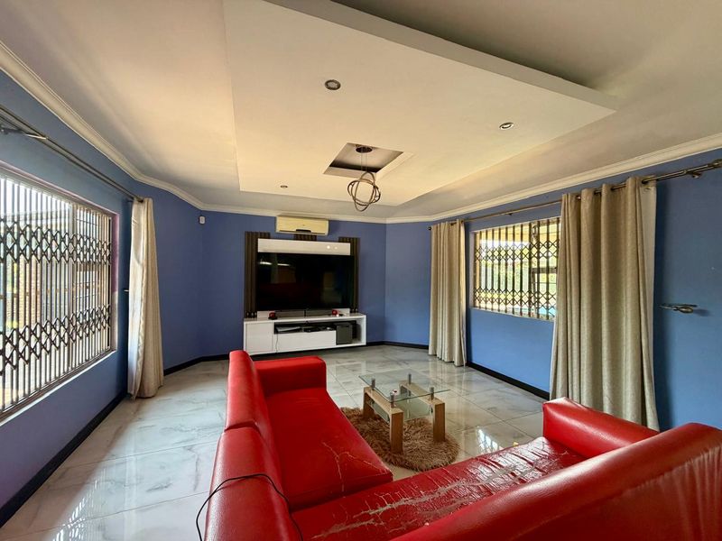 Spacious living room featuring tiled flooring, a recessed ceiling with downlights, a built-in media unit, and security gates on the windows.