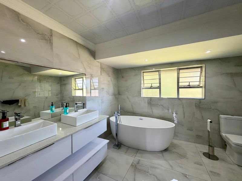 Modern bathroom featuring a double vanity, a sleek freestanding bathtub with floor-mounted filler, and elegant marble-look wall and floor tiling.