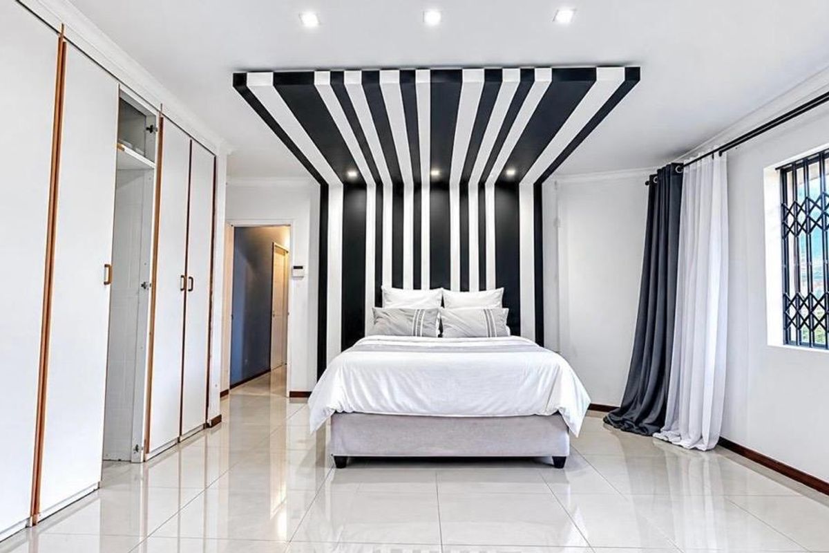 Spacious bedroom featuring large built-in cupboards, polished tiled flooring, and a striking decorative feature wall and ceiling design.