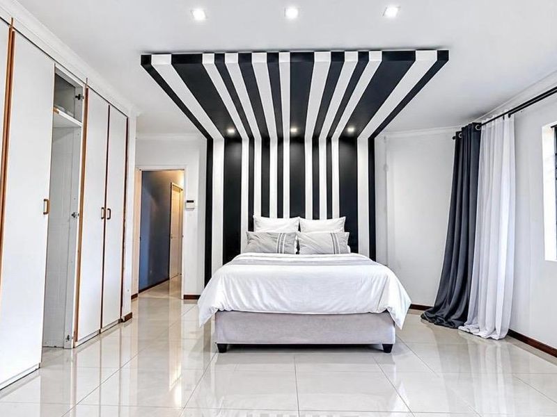 Spacious bedroom featuring large built-in cupboards, polished tiled flooring, and a striking decorative feature wall and ceiling design.