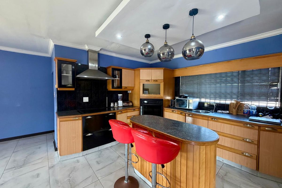 A functional kitchen featuring wooden cabinetry, a central island with breakfast bar, built-in oven, extractor fan, and tiled flooring.