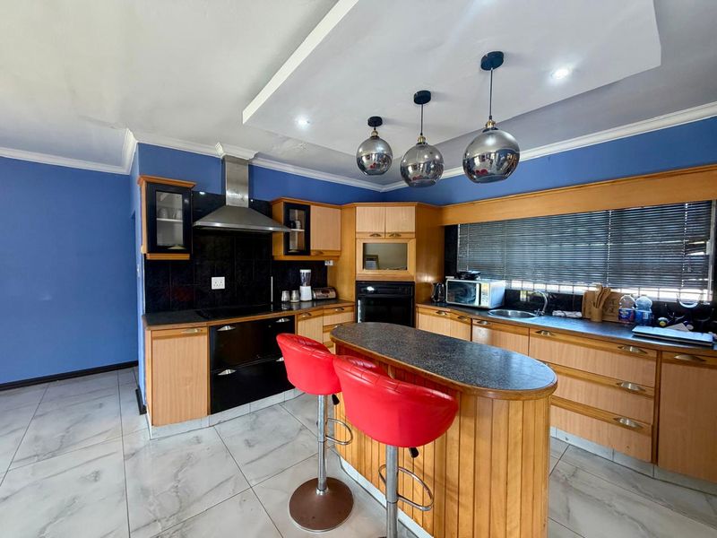 A functional kitchen featuring wooden cabinetry, a central island with breakfast bar, built-in oven, extractor fan, and tiled flooring.