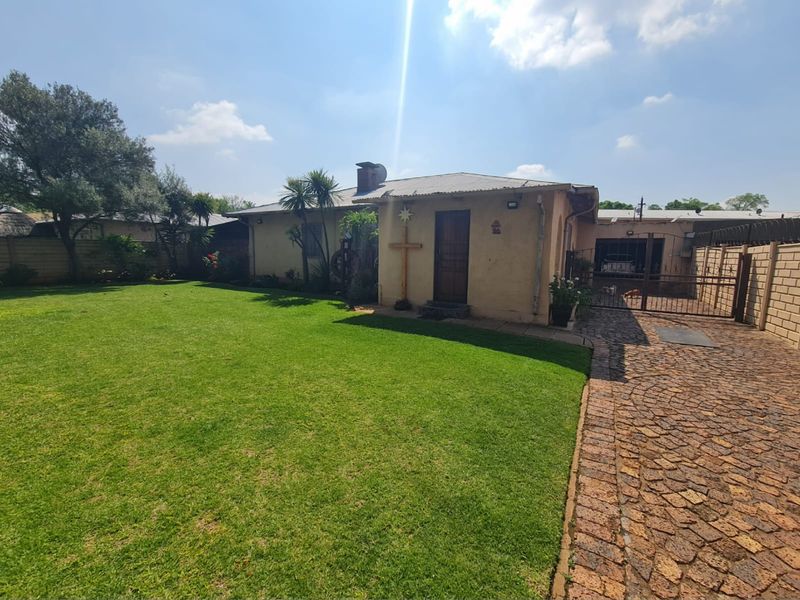 Rear view of the property featuring a spacious lawn, paved driveway, and secure perimeter walling.