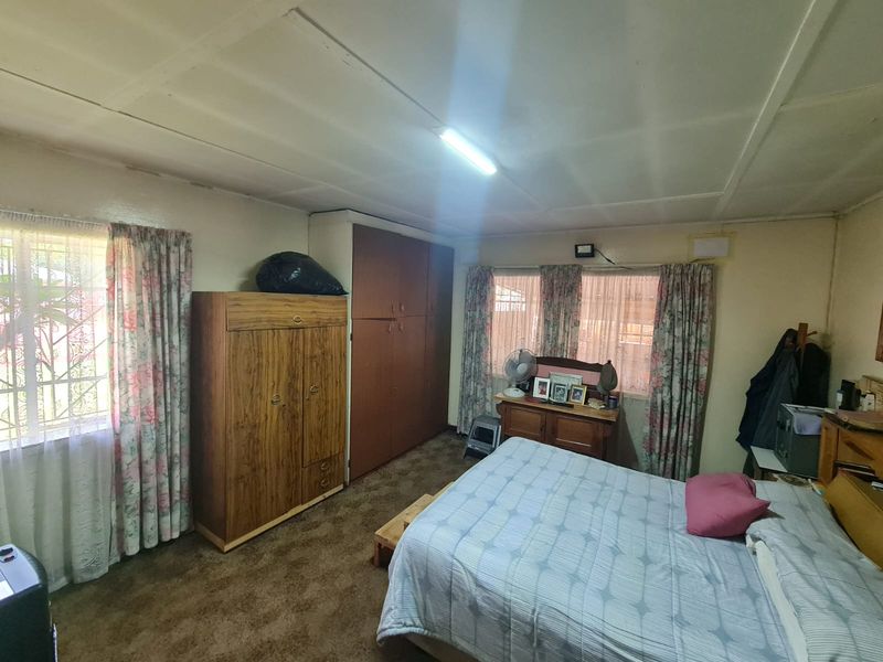 A bedroom featuring built-in cupboards and security bars on the windows, requiring cosmetic updates to the flooring and ceiling finishes.