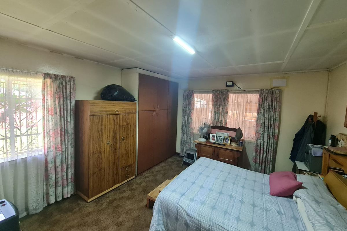 A bedroom featuring built-in cupboards and security bars on the windows, requiring cosmetic updates to the flooring and ceiling finishes.