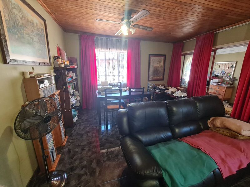 A living room featuring a timber-paneled ceiling, ceiling fan, and dark tiled flooring, offering a functional space with potential for modernization.
