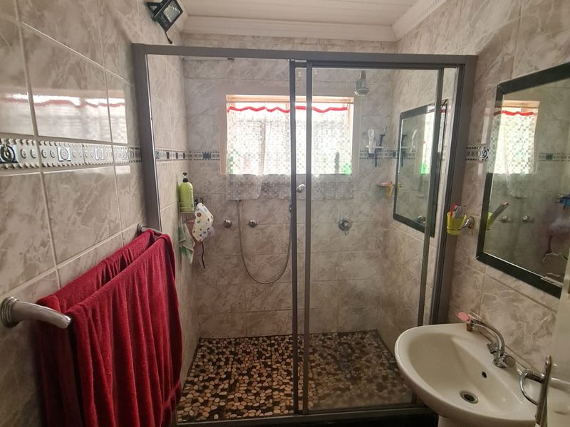 A functional bathroom featuring a pedestal washbasin, a shower enclosure with a pebble-tiled floor, and tiled wall finishes.