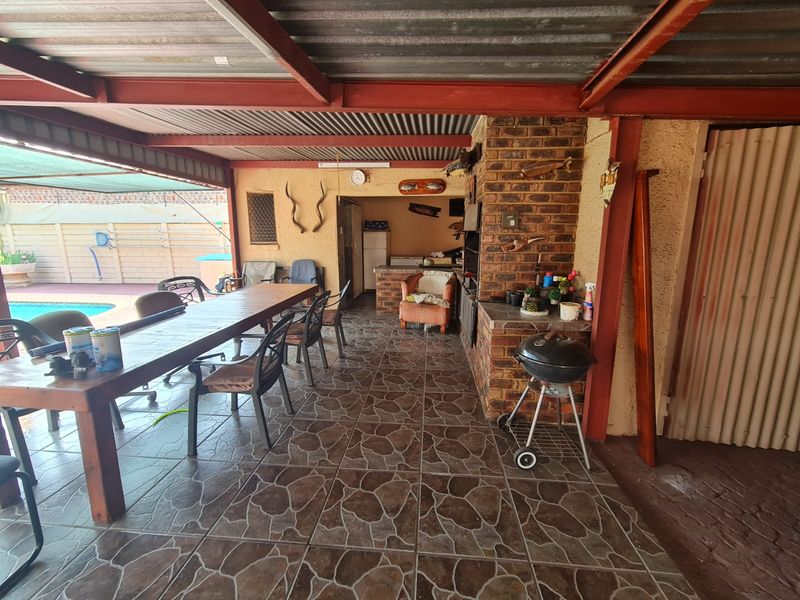 Covered outdoor patio area featuring a built-in brick braai, tiled flooring, and direct access to the garden and pool area.