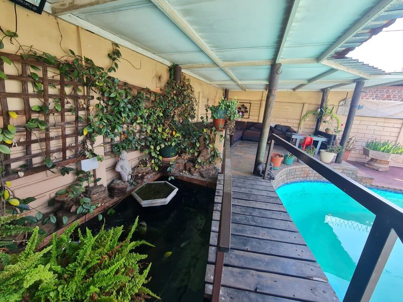 Outdoor pool area featuring a covered patio, a wooden footbridge over a built-in water feature, and established garden trellis elements.