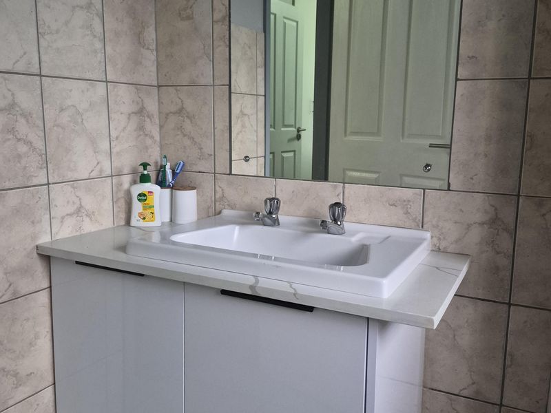 A modern bathroom vanity featuring a wall-mounted cabinet, ceramic basin with chrome mixer, and a large wall-mounted mirror with neutral tiled splashback.