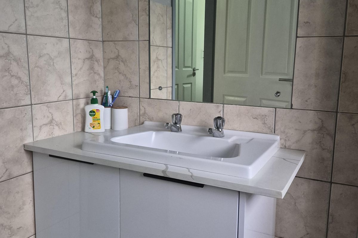 A modern bathroom vanity featuring a wall-mounted cabinet, ceramic basin with chrome mixer, and a large wall-mounted mirror with neutral tiled splashback.