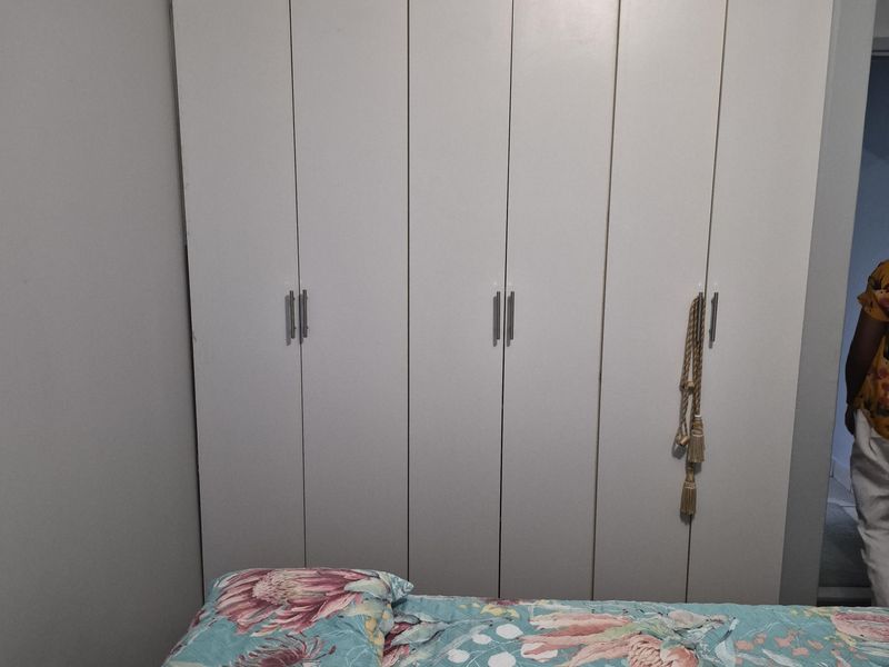 A bedroom featuring a large, white built-in wardrobe with modern handles and decorative cove cornicing.