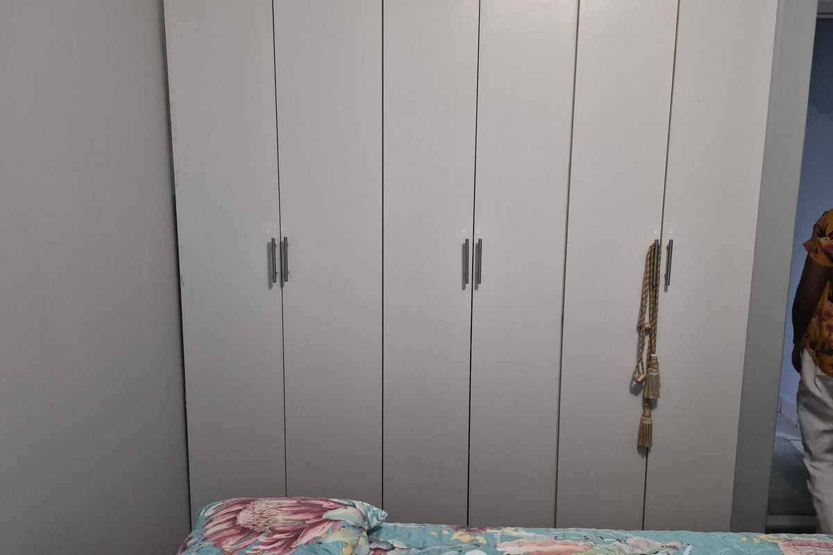 A bedroom featuring a large, white built-in wardrobe with modern handles and decorative cove cornicing.