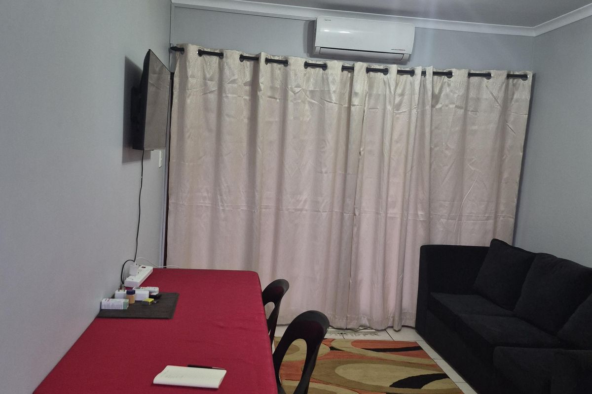 A functional living area featuring tiled flooring, a wall-mounted air conditioning unit, and neutral wall finishes.