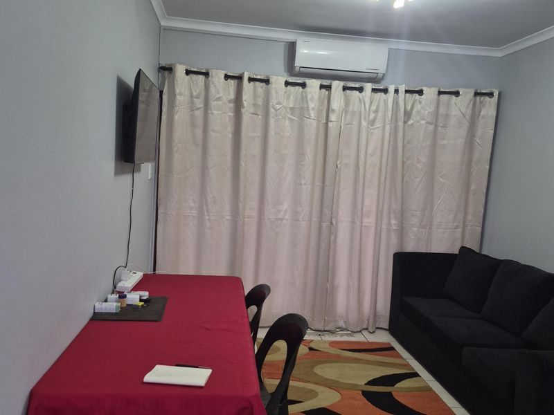 A functional living area featuring tiled flooring, a wall-mounted air conditioning unit, and neutral wall finishes.