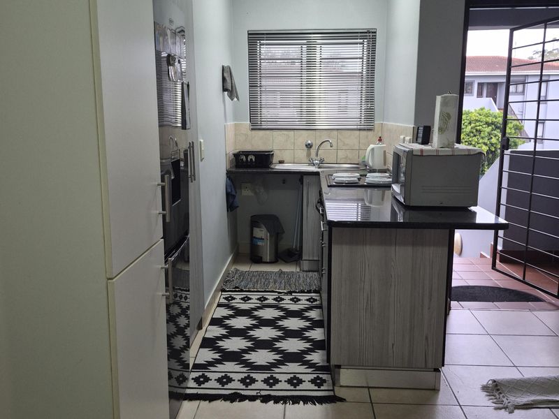 A functional kitchen featuring granite countertops, built-in cabinetry, and tiled flooring, with direct access to an outdoor area through a security gate.