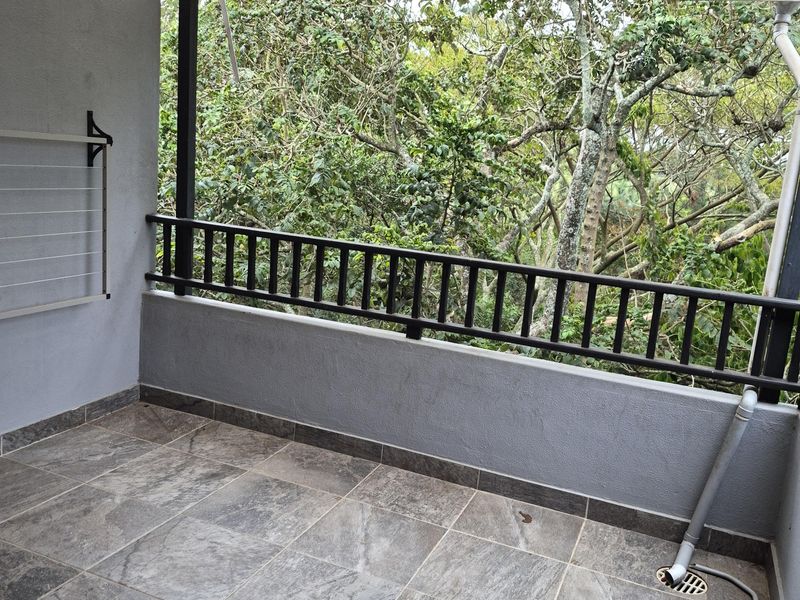 A covered balcony featuring tiled flooring, a timber pergola, and a metal balustrade, offering a private outdoor space with a leafy outlook.