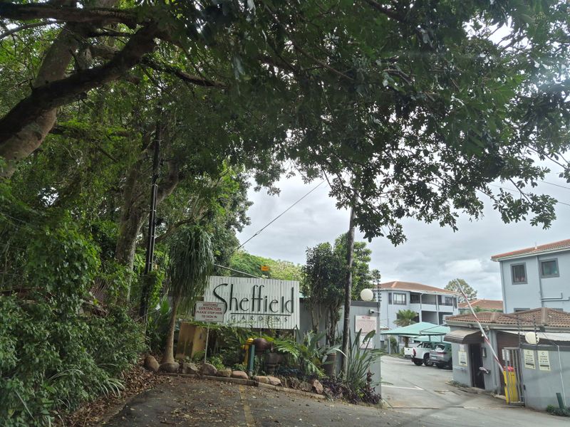Entrance view of Sheffield Gardens apartment complex featuring a security gate, signage, and paved driveway access.