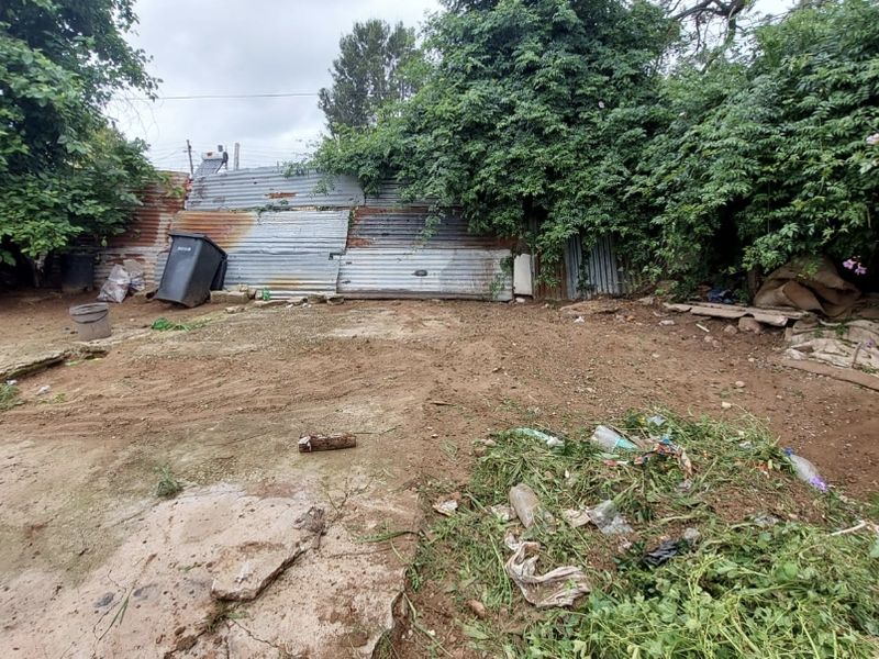 Rear outdoor area featuring corrugated metal fencing and unmaintained ground, offering potential for landscaping or garden development.