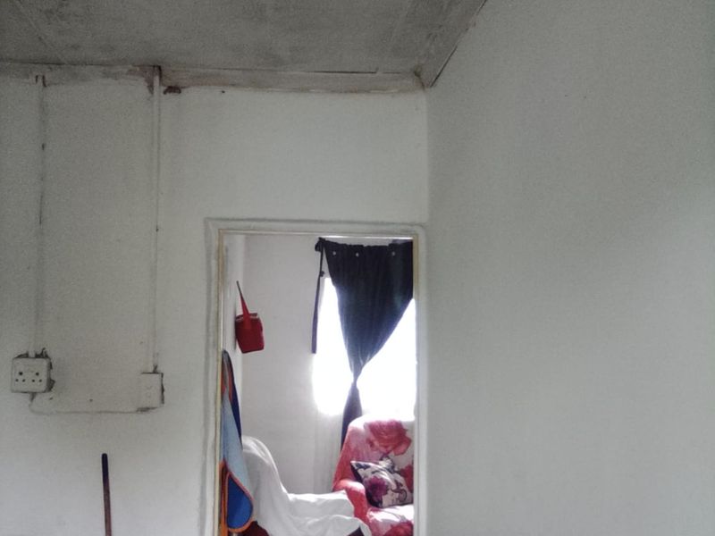 A utility or laundry area featuring exposed electrical conduit and an unfinished concrete ceiling, leading into an adjacent room.