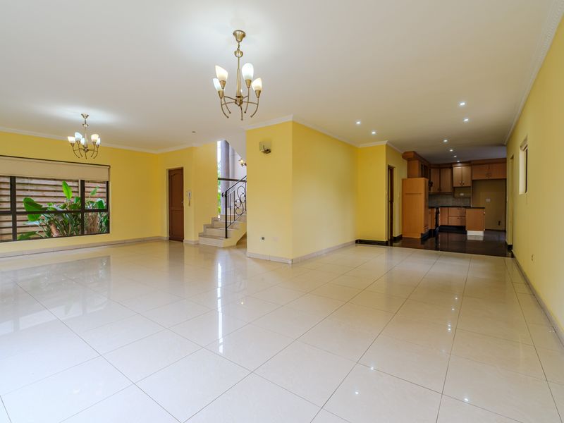 Spacious open-plan living and kitchen area featuring tiled floors, recessed lighting, and a staircase with wrought iron detailing.