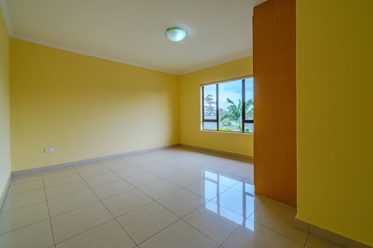 A bright, empty bedroom featuring neutral tiled flooring, yellow walls, and a built-in cupboard, offering a clean and versatile space.